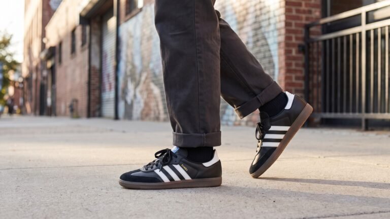 Person walking on a city sidewalk wearing black Adidas Samba sneakers with classic white stripes and gum soles