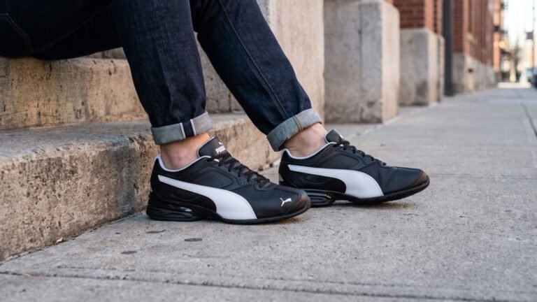 Black and white Puma Tazon 6 sneakers worn with cuffed dark jeans on outdoor concrete steps