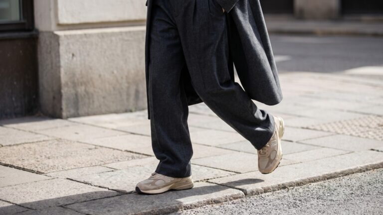 Person walking in charcoal wide-leg trousers paired with beige retro running sneakers on a city sidewalk