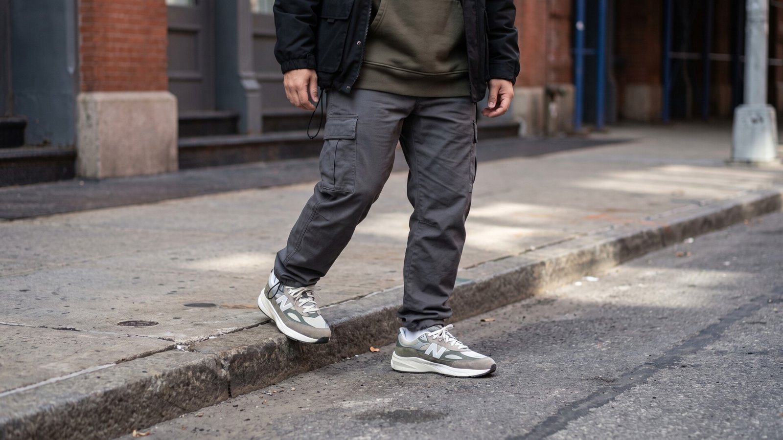 Person wearing grey cargo trousers and neutral athletic sneakers stepping off a city sidewalk curb