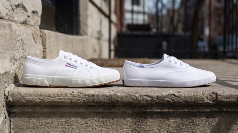 White Superga 2750 sneaker next to a white Keds Champion sneaker resting on an outdoor stone ledge