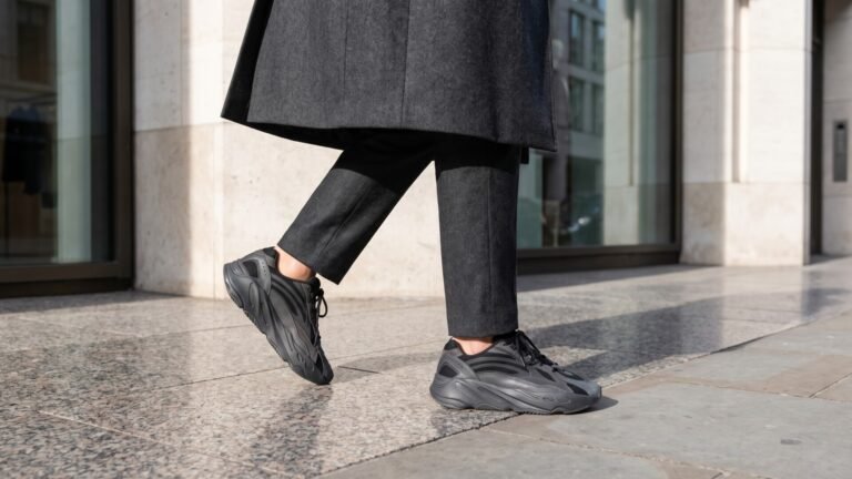 Low-angle view of tailored charcoal wool trousers paired with dark chunky luxury sneakers walking on a city sidewalk