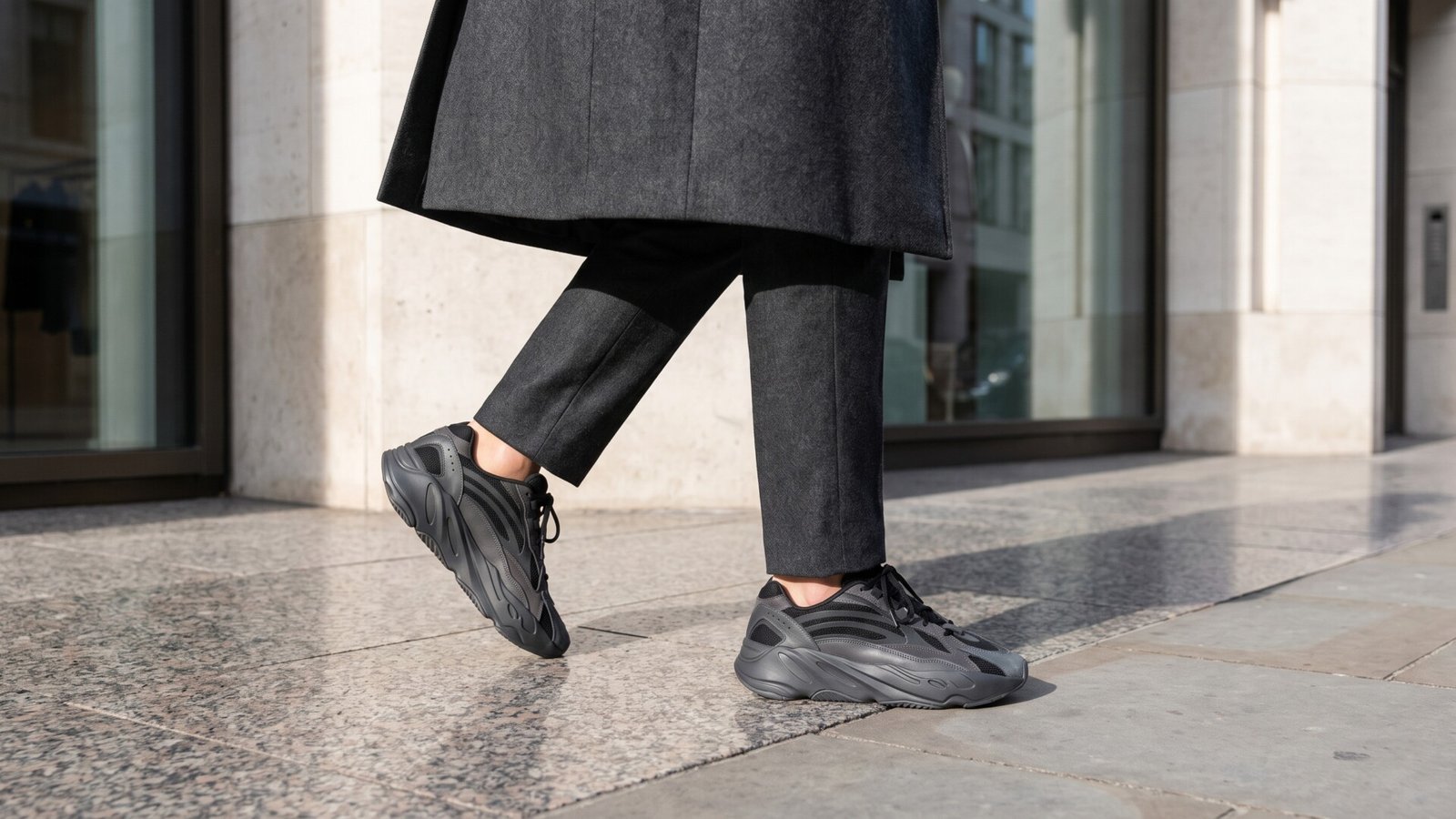 Low-angle view of tailored charcoal wool trousers paired with dark chunky luxury sneakers walking on a city sidewalk