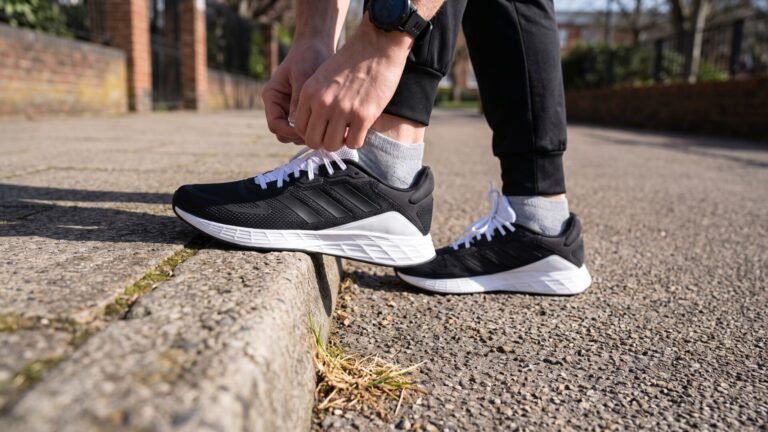 Runner tying the white laces of a black Adidas Duramo SL sneaker on a concrete curb