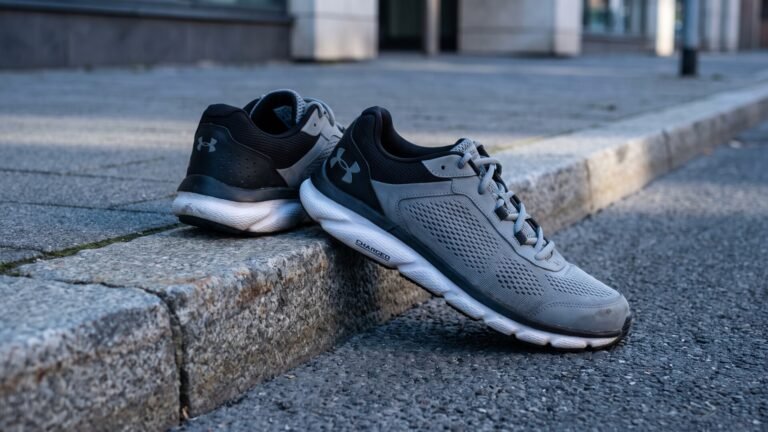 Grey and black Under Armour Charged running shoes resting against a street curb