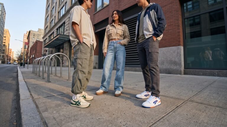 Three young adults showcasing spring streetwear outfits, relaxed cargo pants, and retro sneakers on a city sidewalk