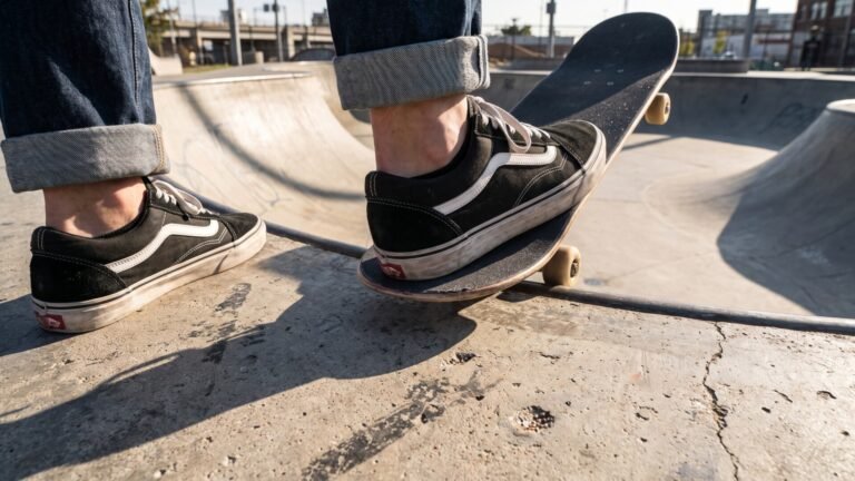 Skater wearing black Vans Old Skool sneakers balancing on a skateboard at the edge of a concrete skate bowl