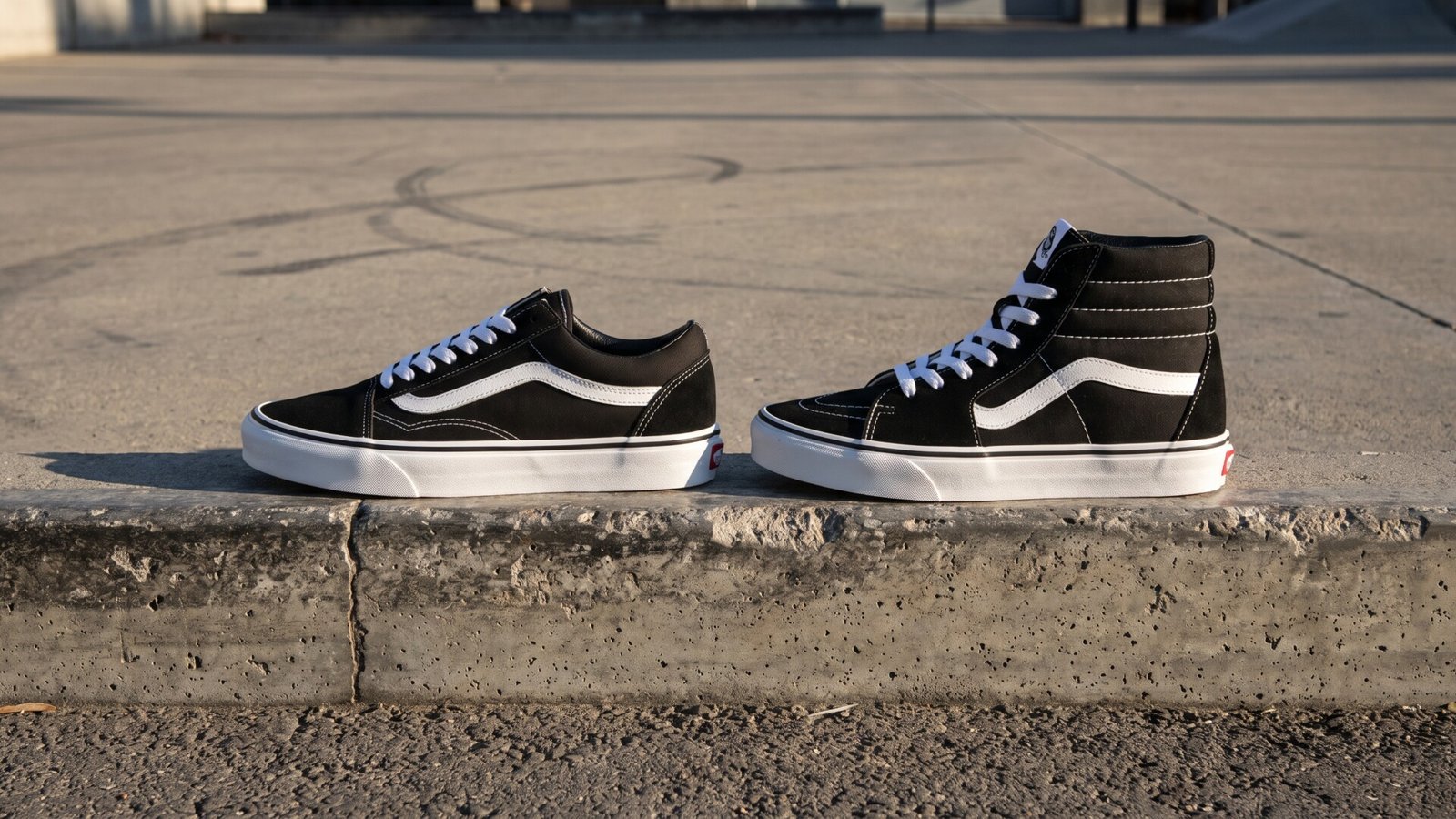Side-by-side profile view of a black and white Vans Old Skool low-top and a Vans Sk8-Hi high-top sneaker on a concrete curb