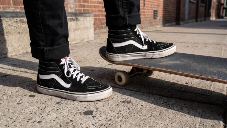 Classic black and white Vans Sk8-Hi sneakers worn by a skater with one foot resting on a skateboard