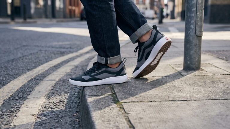 Black and grey Vans UltraRange EXO sneakers worn with cuffed jeans on a city sidewalk curb