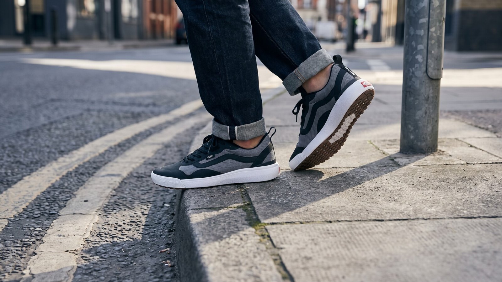 Black and grey Vans UltraRange EXO sneakers worn with cuffed jeans on a city sidewalk curb