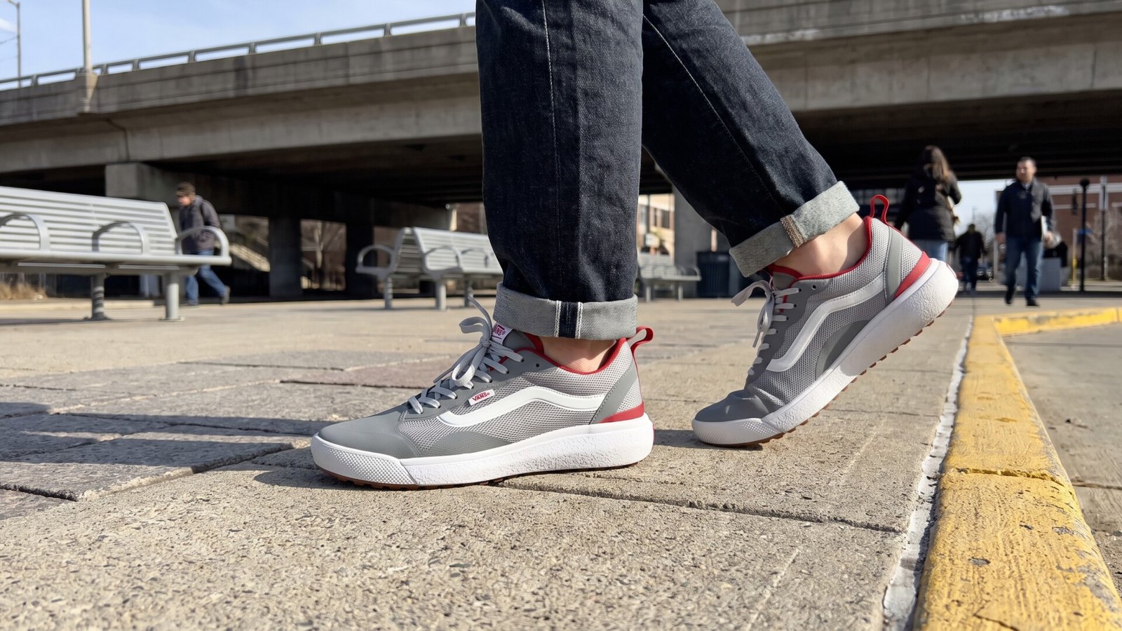 Person wearing grey and red Vans UltraRange sneakers mid-stride across an urban transit plaza