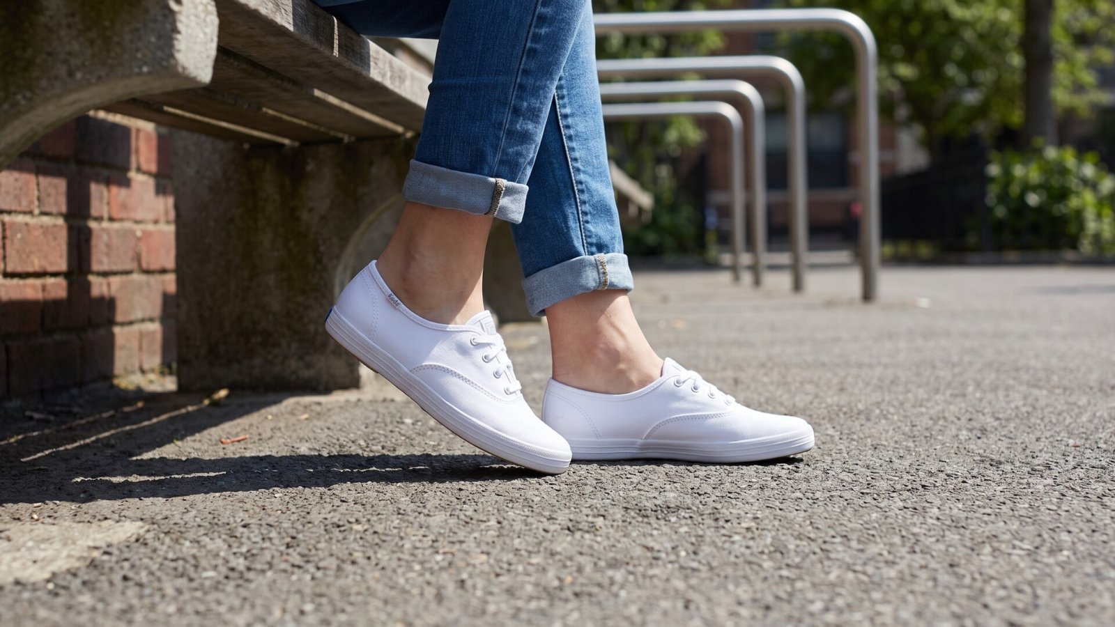 Person wearing white Keds Champion Canvas sneakers with cuffed blue jeans while sitting on an outdoor bench